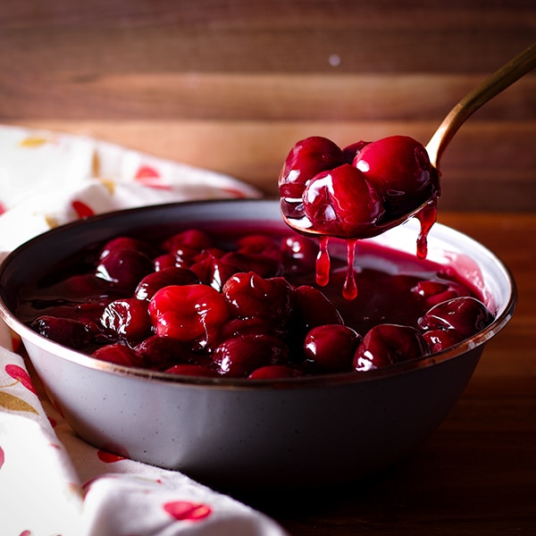 A gold spoon scooping out a spoonful of cherry sauce.