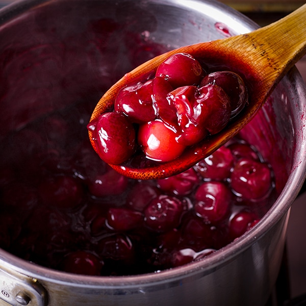 A wooden spoon holding up a spoonful of cherry sauce over a saucepan.