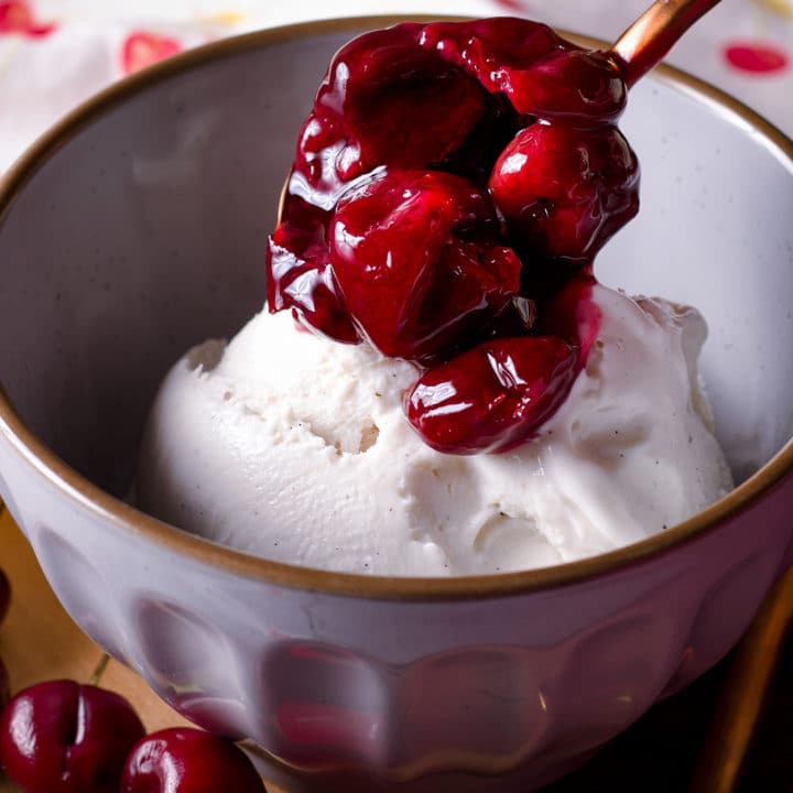 Spooning cherry sauce over a bowl of vanilla ice cream.