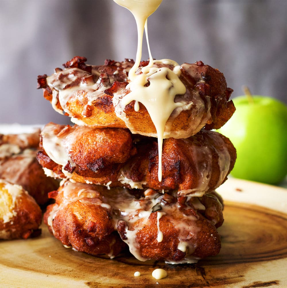 Maple glaze dripping down the side of a stack of three homemade apple fritters.