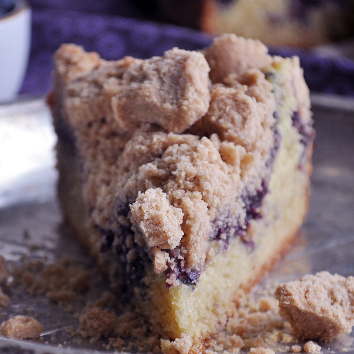 A slice of blueberry crumb cake on a tin plate.
