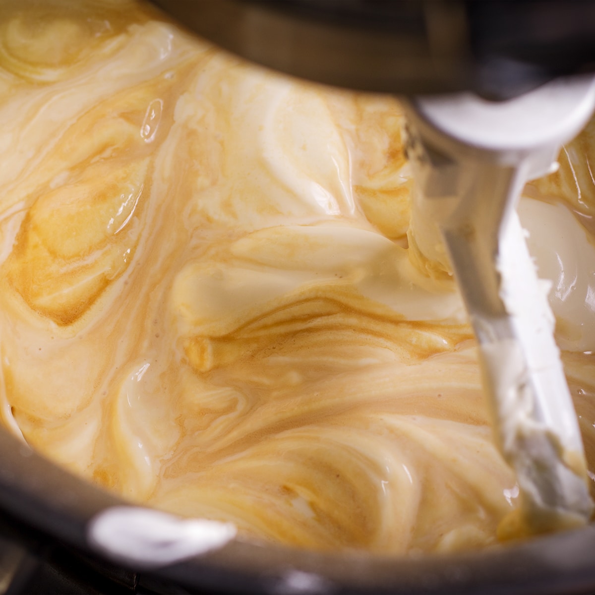 Using an electric mixer to beat vanilla and heavy cream into cheesecake batter.