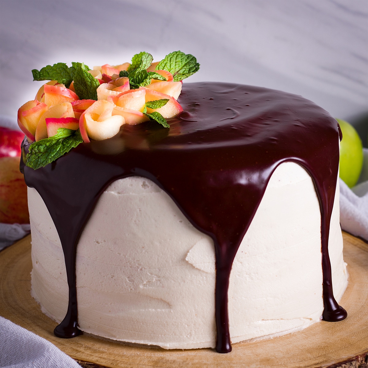 A frosted layer cake topped with chocolate ganache and decorated with apple roses.