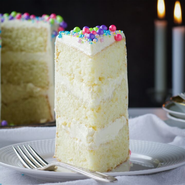 A slice of Buttercream Frosted Vanilla Layer Cake on a plate with a fork.
