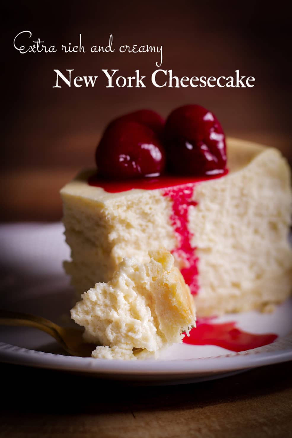 A thick slice of New York Cheesecake with cherry sauce on top on a white plate with a gold fork.