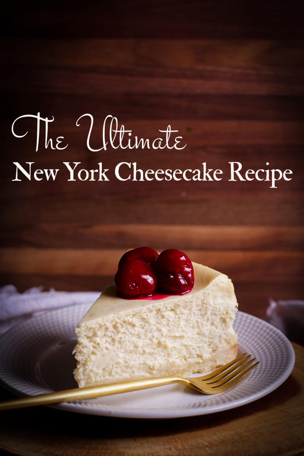 A thick slice of New York Cheesecake with cherry sauce on top on a white plate with a gold fork.