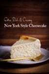 A thick slice of New York Cheesecake on a white plate with a gold fork.