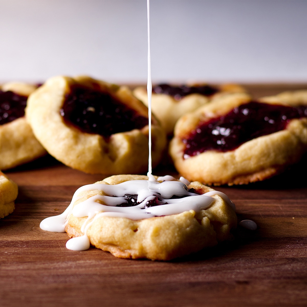 Drizzling vanilla glaze over almond thumbprint cookies filled with cherry preserves.