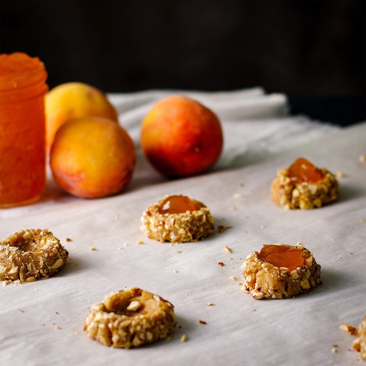 A baking sheet with almond thumbprint cookies that are being filled with peach preserves.