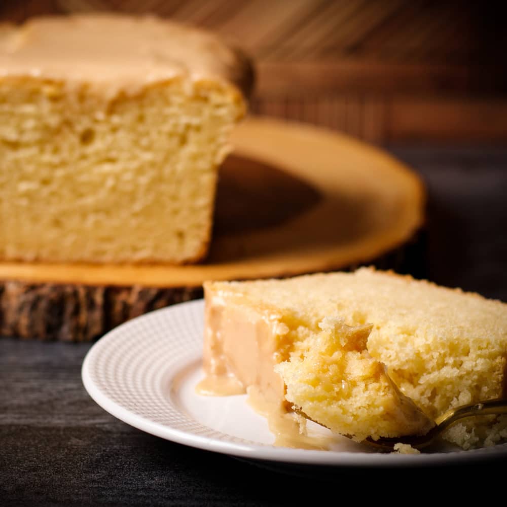 A slice of Vanilla Loaf Cake on a white plate with a bite of cake on a gold fork.