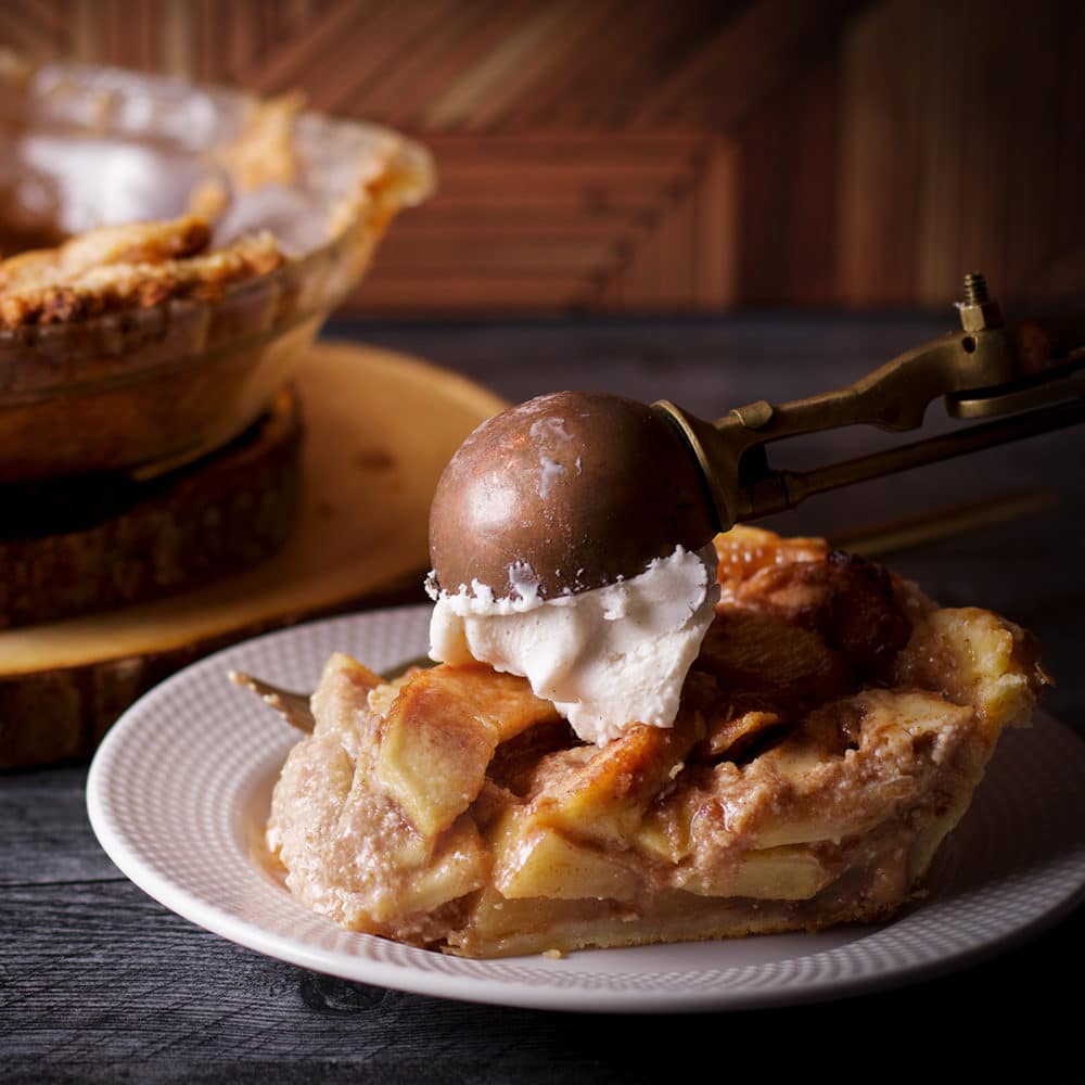 Using an ice cream scoop to top a slice of German Apple Pie with a scoop of vanilla ice cream.