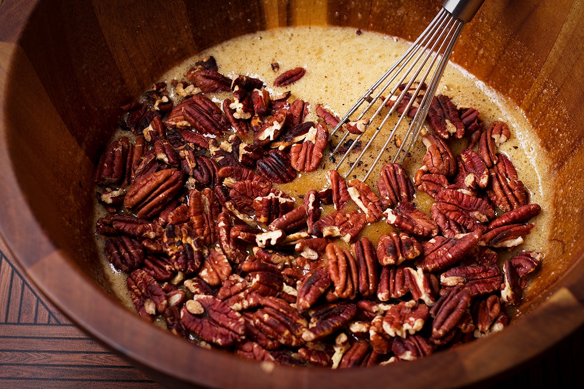 Someone using a wire whisk to stir toasted pecans into the other ingredients for pecan pie filling.