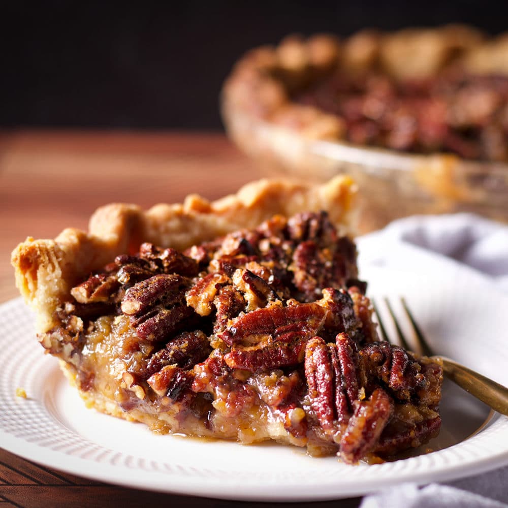 A slice of pecan pie on a white plate with a gold fork.