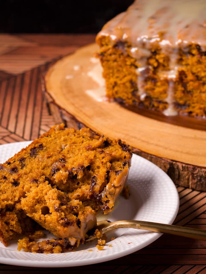 A slice of pumpkin chocolate chip bread on a white plate with a bite resting on a gold fork.