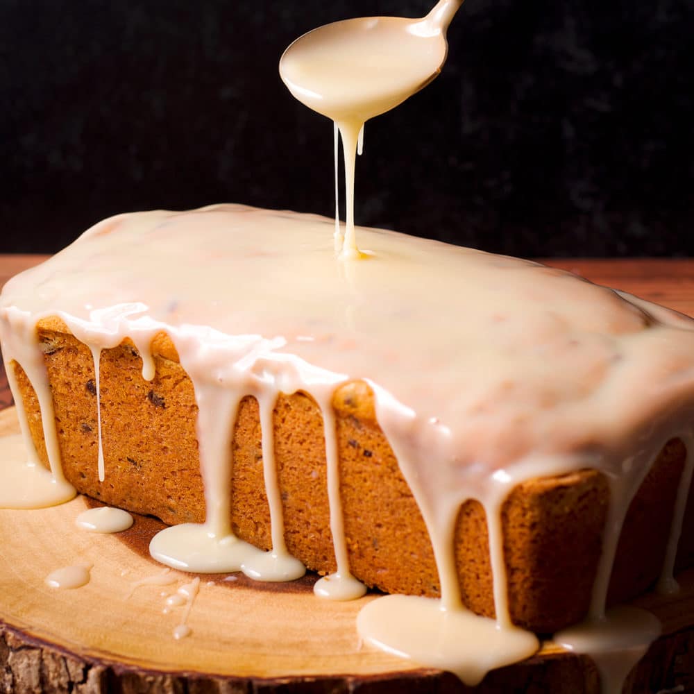 Using a spoon to drizzle white chocolate glaze over a loaf of pumpkin chocolate chip bread.