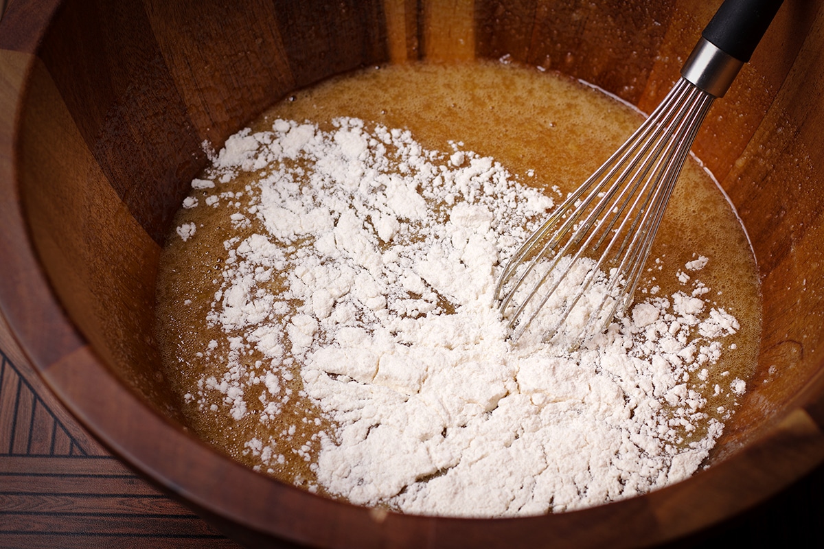 Someone using a wire whisk to mix flour into the rest of the pecan pie filling ingredients.