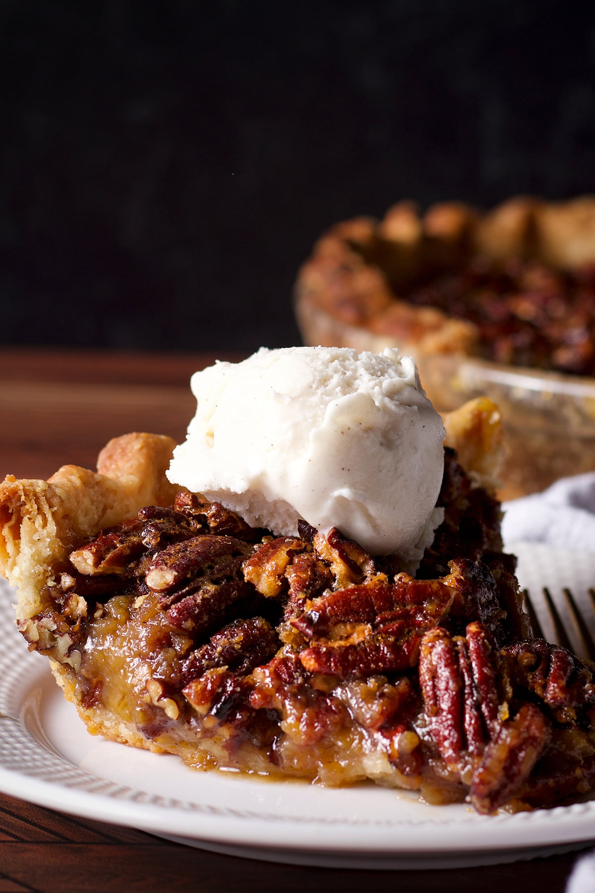 A slice of pecan pie topped with a scoop of vanilla ice cream.