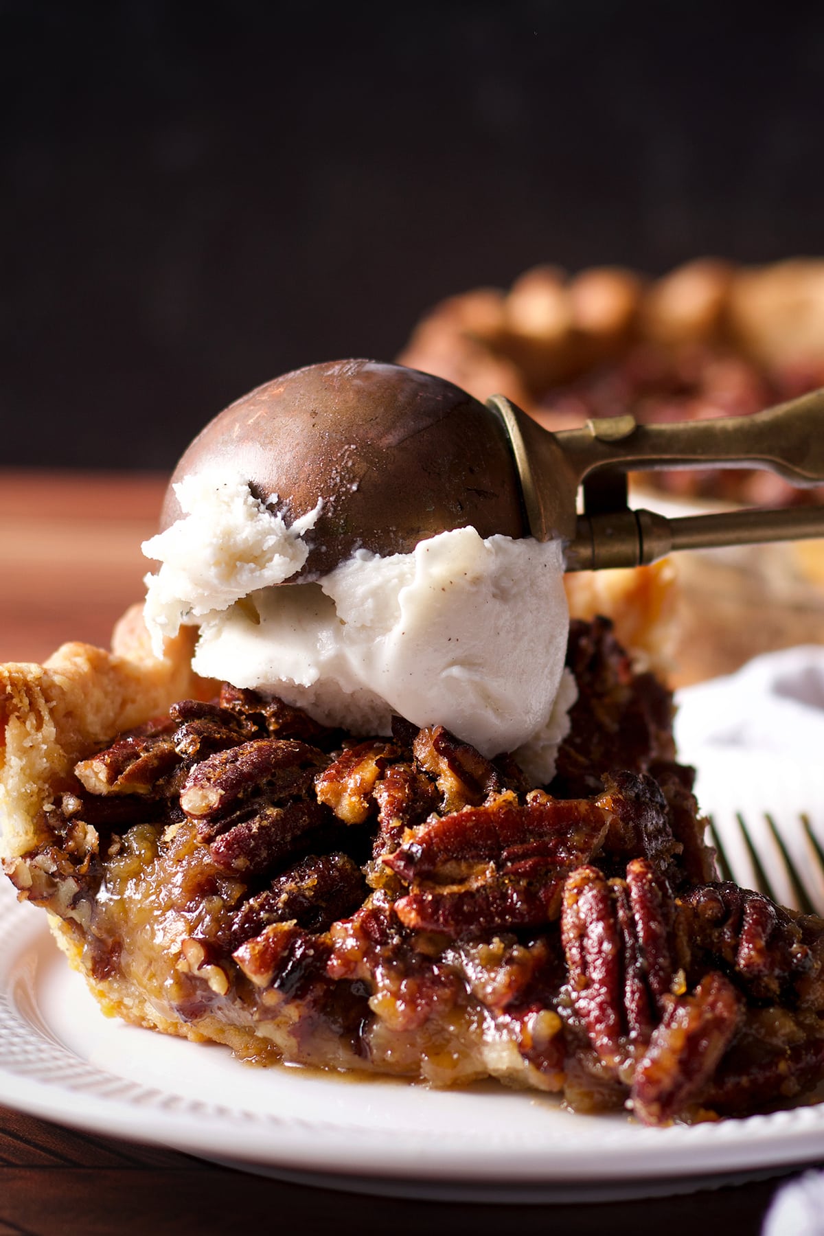 Someone using an old fashioned ice cream scoop to top a slice of pecan pie with vanilla ice cream.