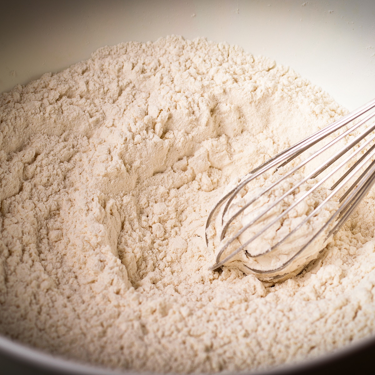 Using a wire whisk to stir flour, baking soda, cornstarch and salt in a white bowl.