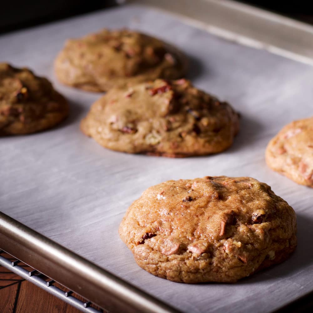 A tray of freshly baked chocolate chip pecan cookies on a baking sheet.