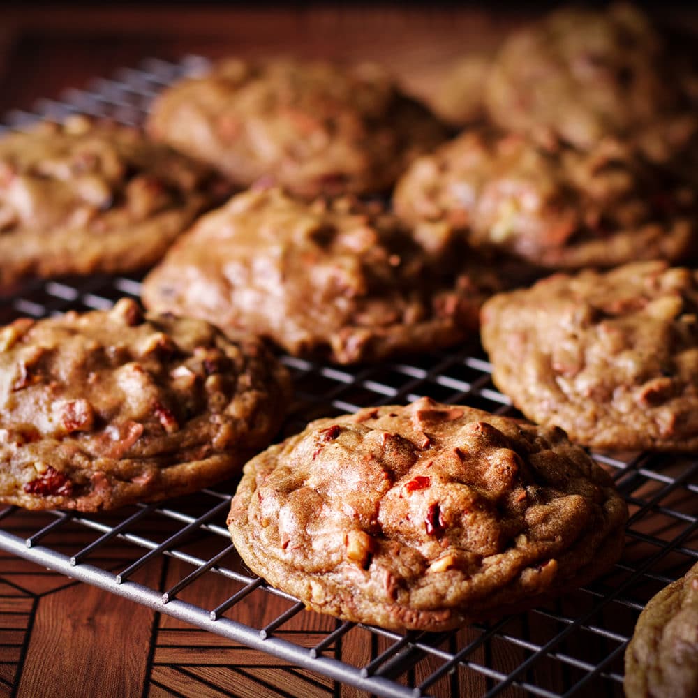 A wire wrack with freshly baked chocolate chip pecan cookies cooling on it.