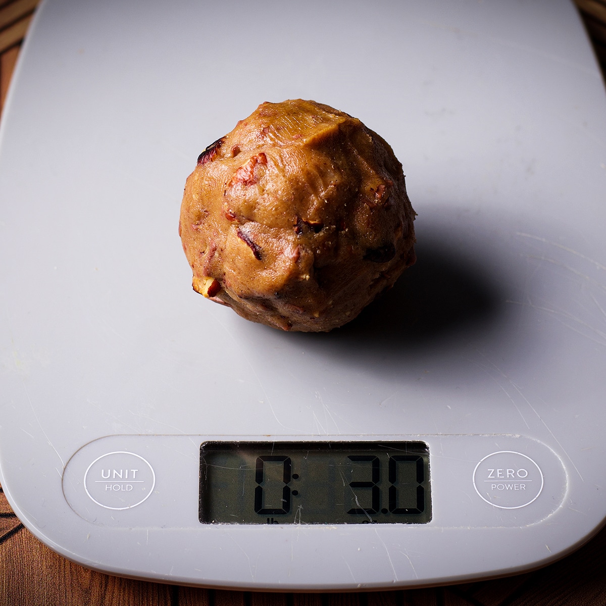 A ball of chocolate chip pecan cookie dough on a scale showing the weight of the cookie dough at 3 ounces.