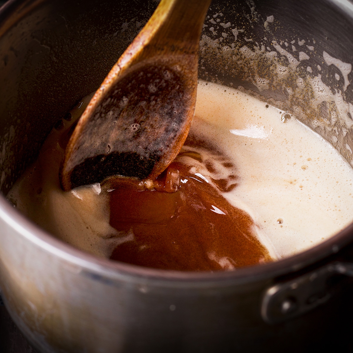 Someone using a wood spoon to stir browned butter in a saucepan.