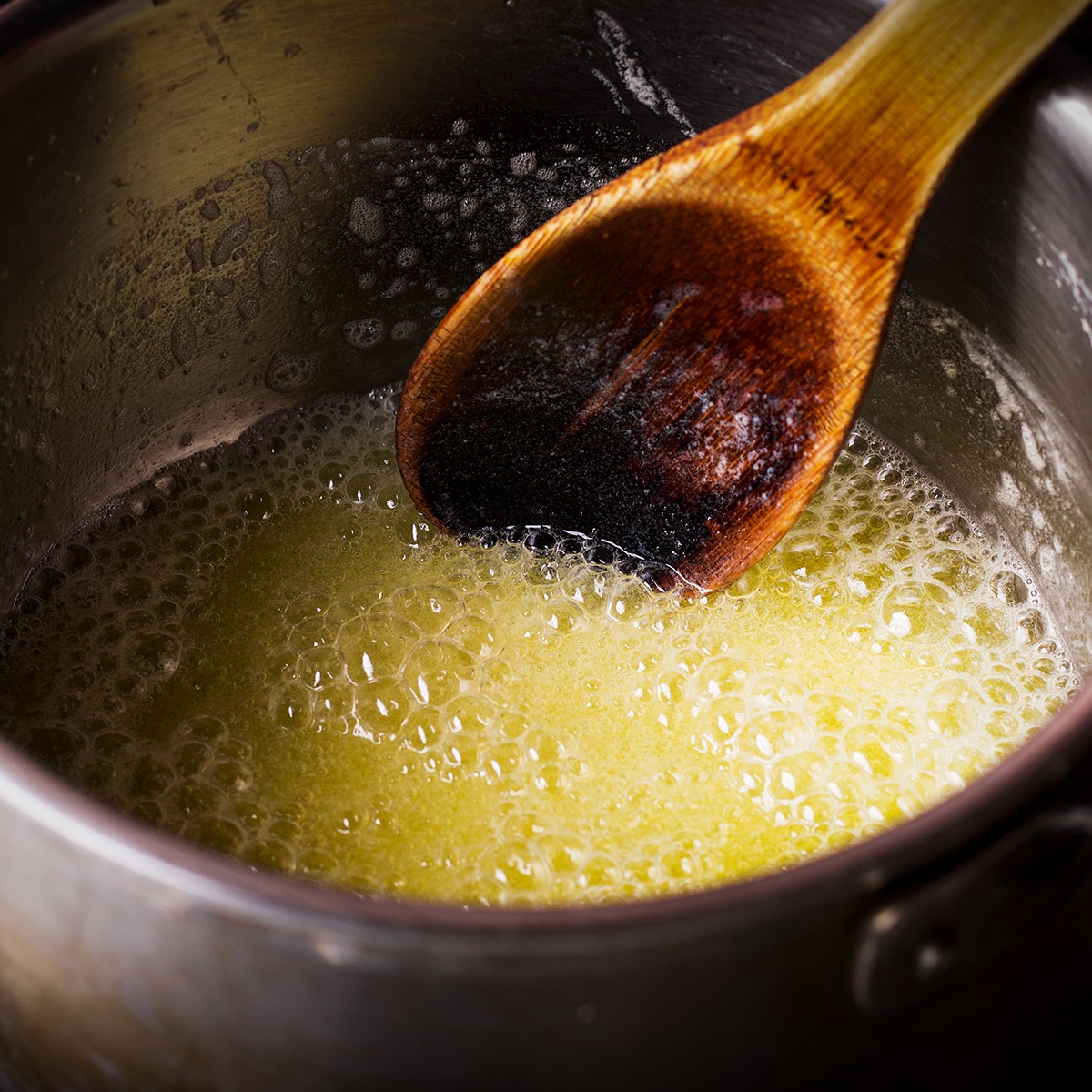 Someone using a wood spoon to stir melted, boiling butter in a saucepan.