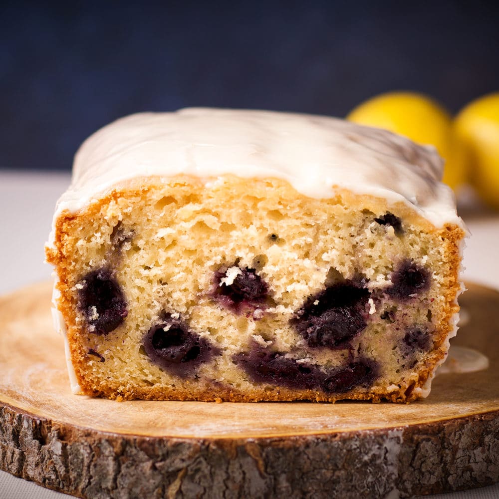 A blueberry loaf cake on a wood cutting board that's been cut in half so you can see inside the loaf.