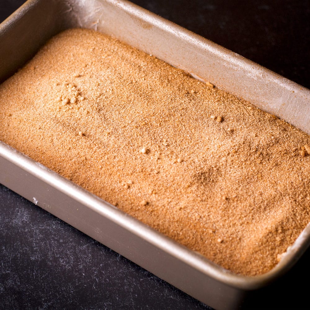 A loaf pan that contains layers of cake batter and cinnamon sugar.