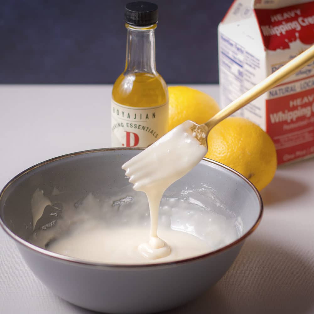 Lifting a fork from a bowl of lemon icing to show a pourable consistency.