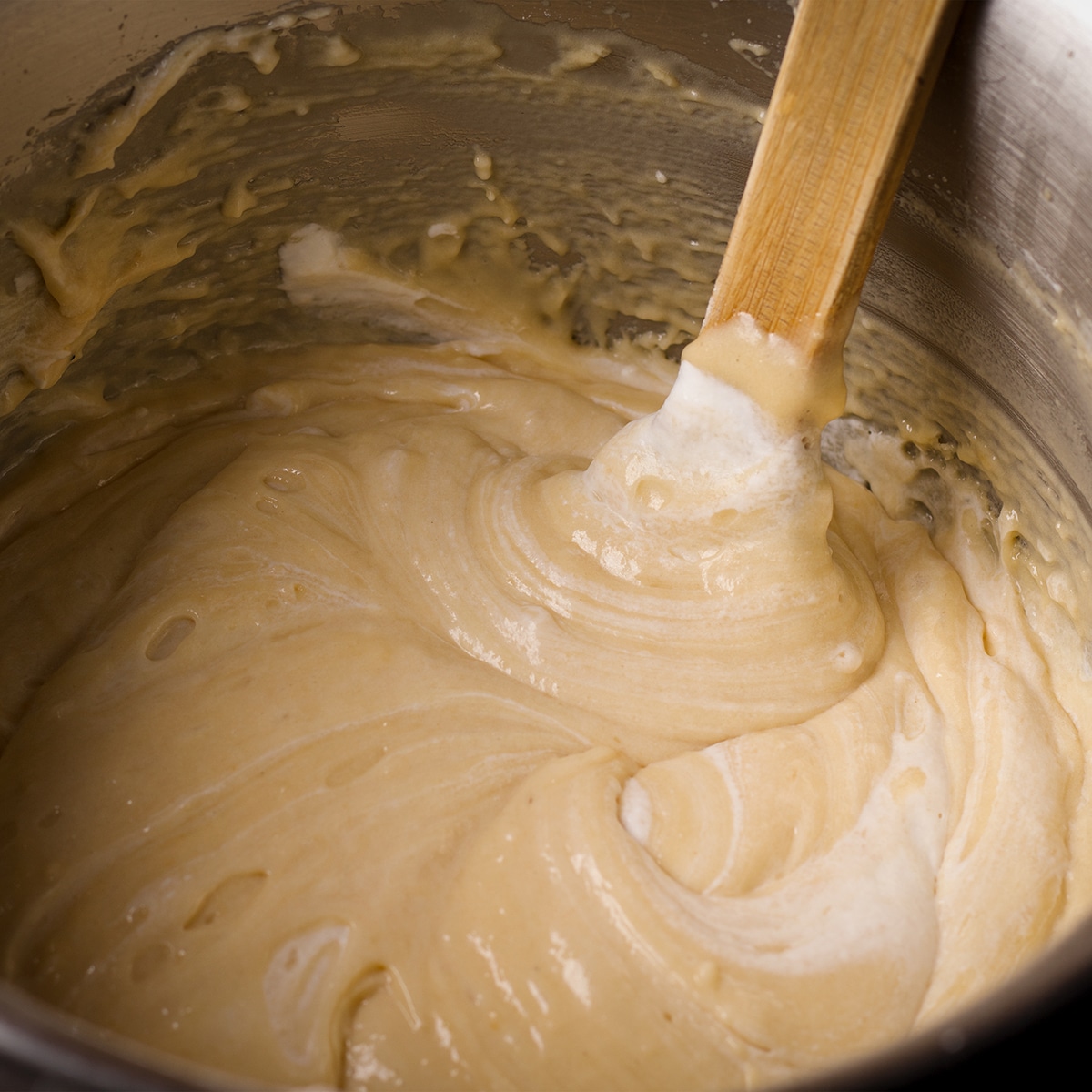 Using a wooden spoon to gently fold whipped cream into the loaf cake batter.