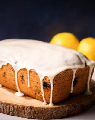 A blueberry loaf cake covered in lemon icing on a wood serving tray.