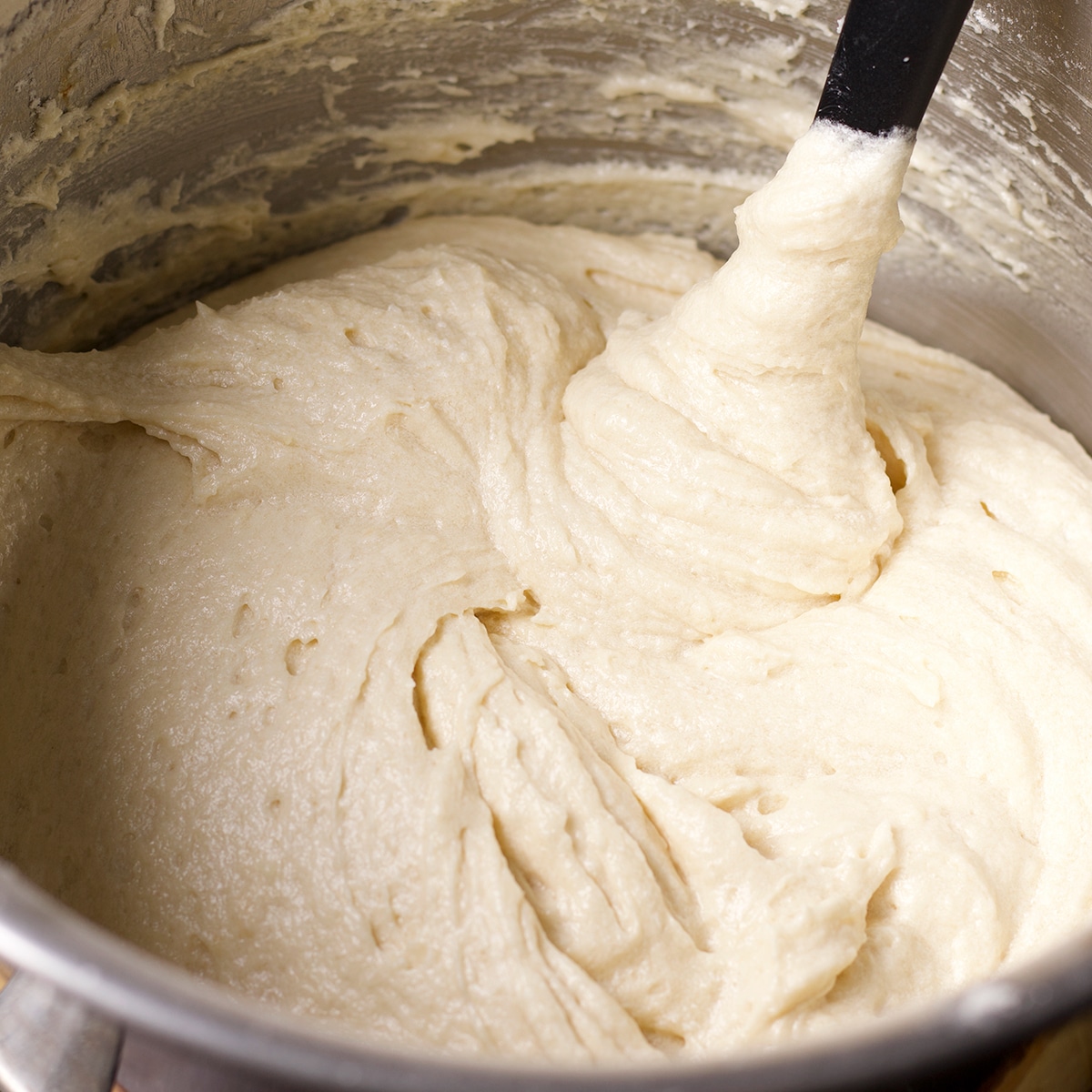 Someone using a rubber spatula to stir cake batter in a bowl.