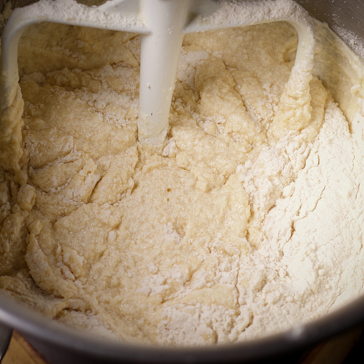Adding flour and milk to a stand mixing bowl that's been fitted with the paddle attachment.