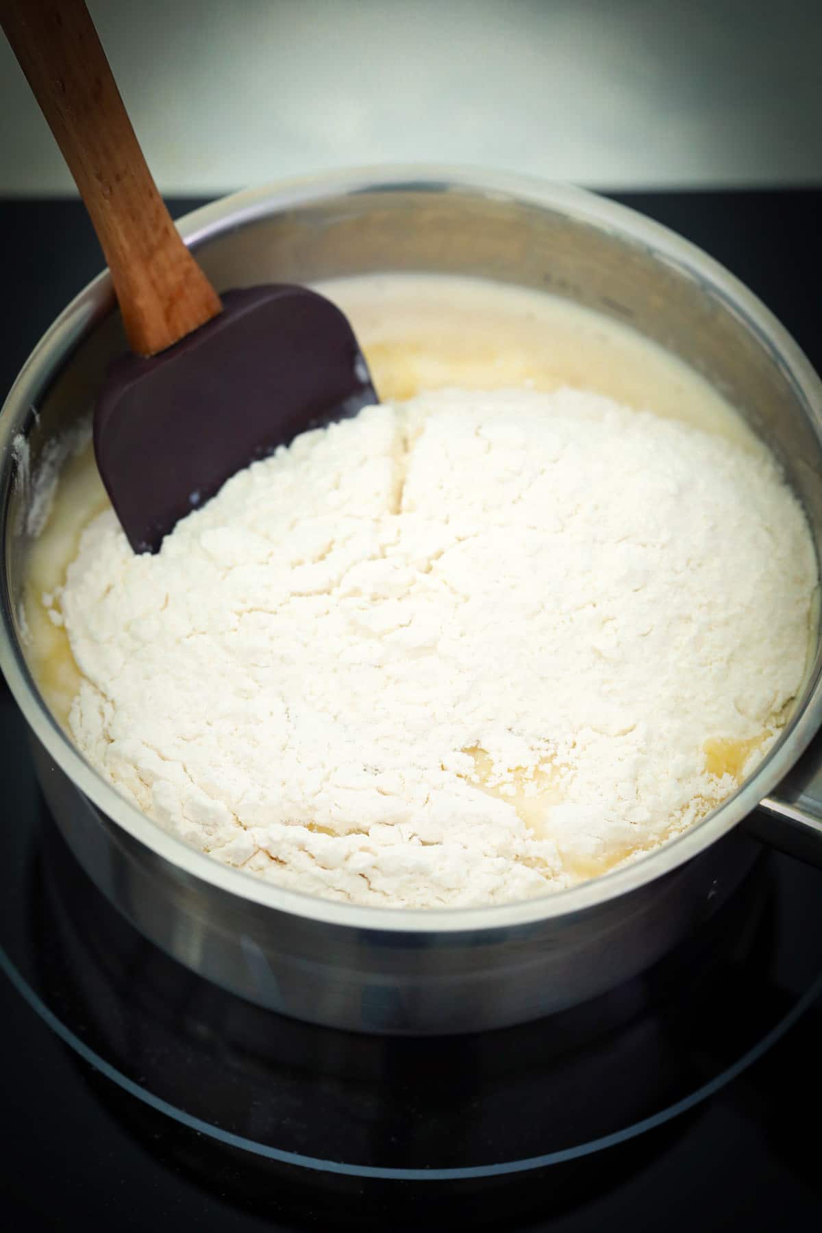 A photo that shows adding the flour to boiling butter and milk then stirring it to make choux pastry dough.