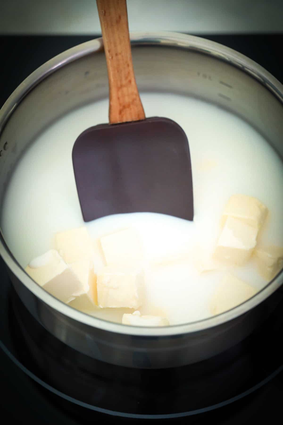 Someone using a spatula to stir milk and butter in a saucepan.