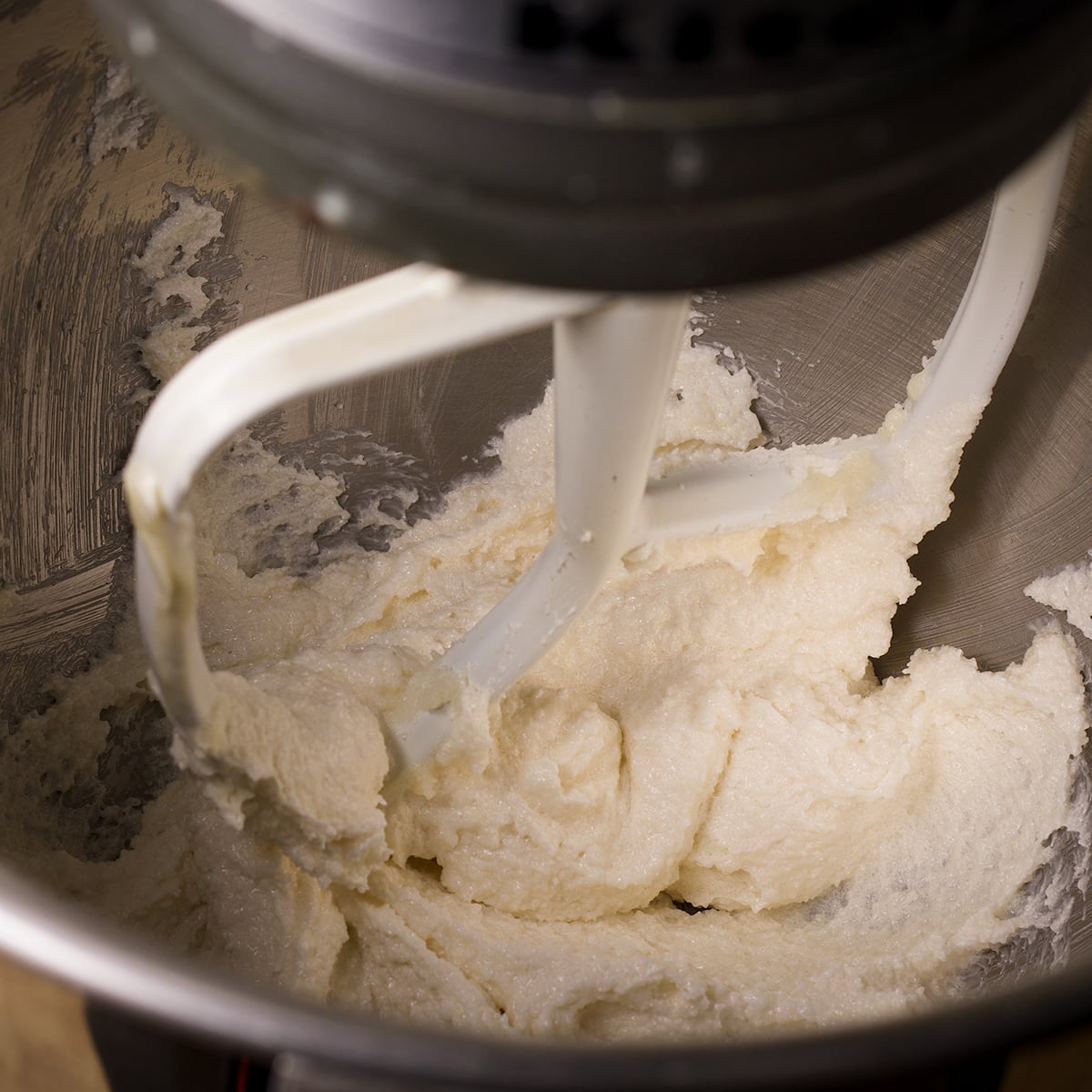 Looking inside the bowl of an electric stand mixer beating butter and sugar until the consistency is light and fluffy.