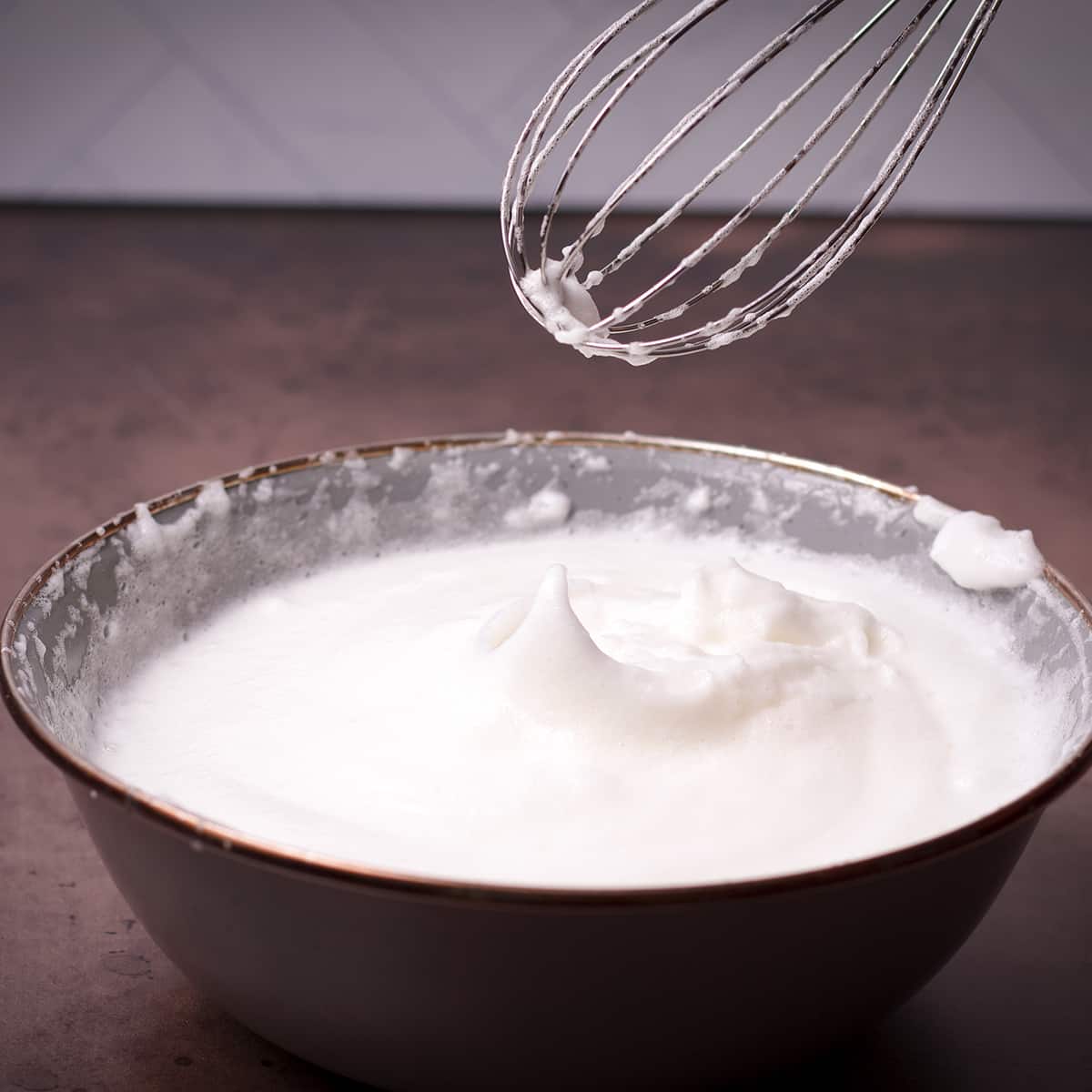 Someone lifting a whisk from a bowl of beaten egg whites to show that the egg whites are at the stiff peak stage.