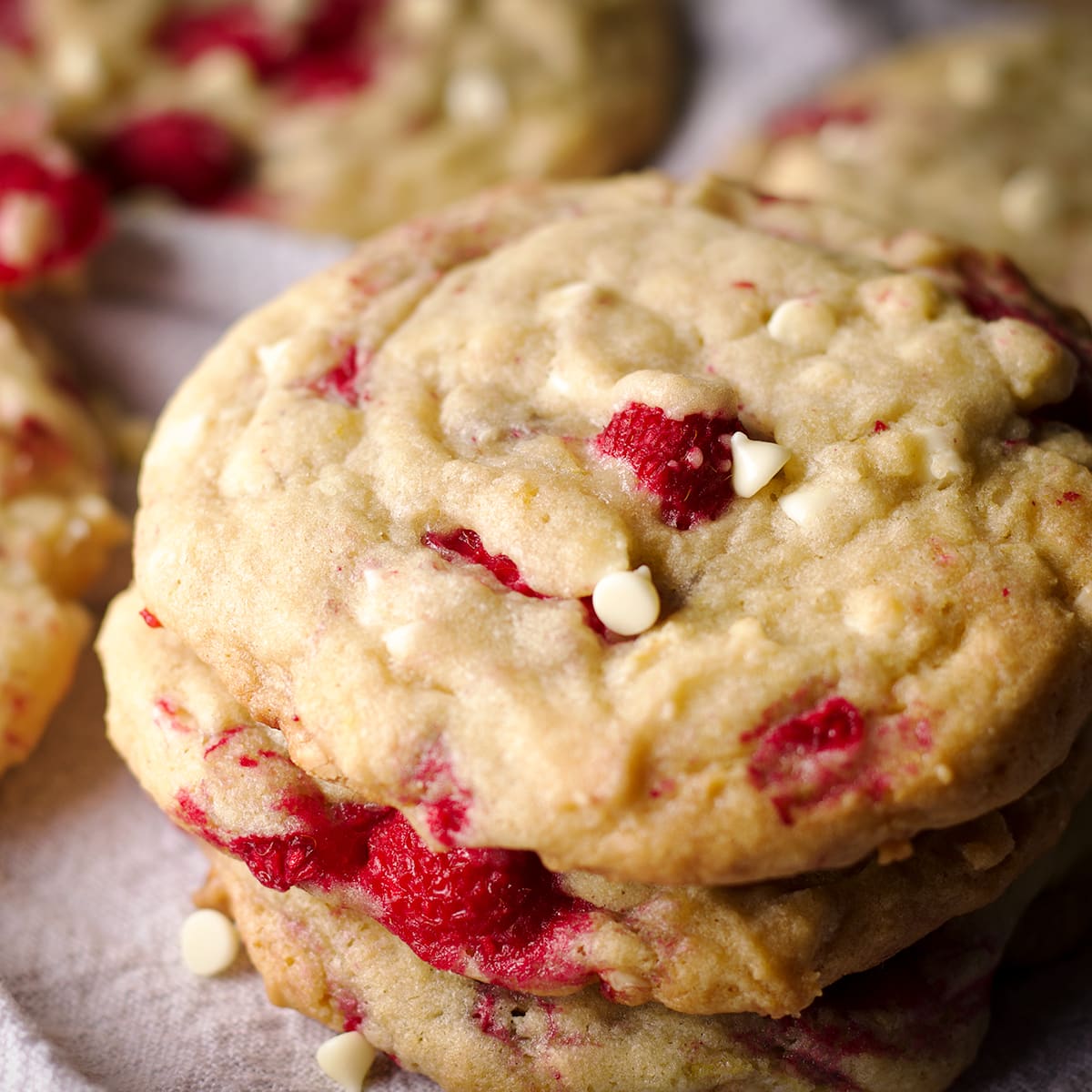 A close up photo of a stack of three white chocolate raspberry cookies.