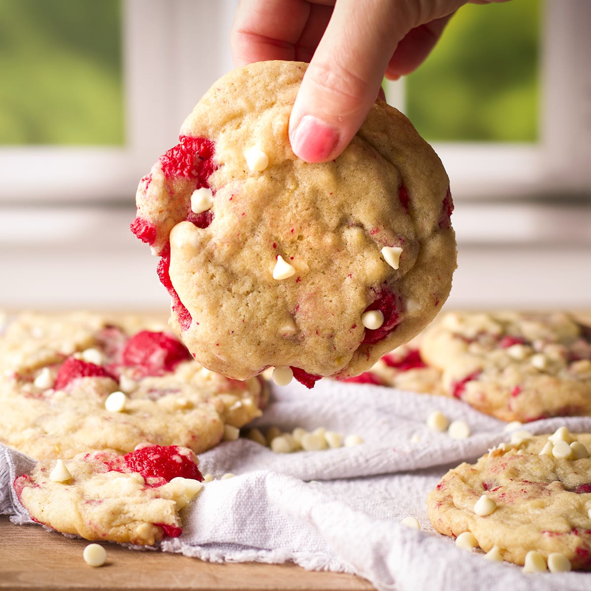 Someone lifting a white chocolate raspberry cookie from a tray of cookies.