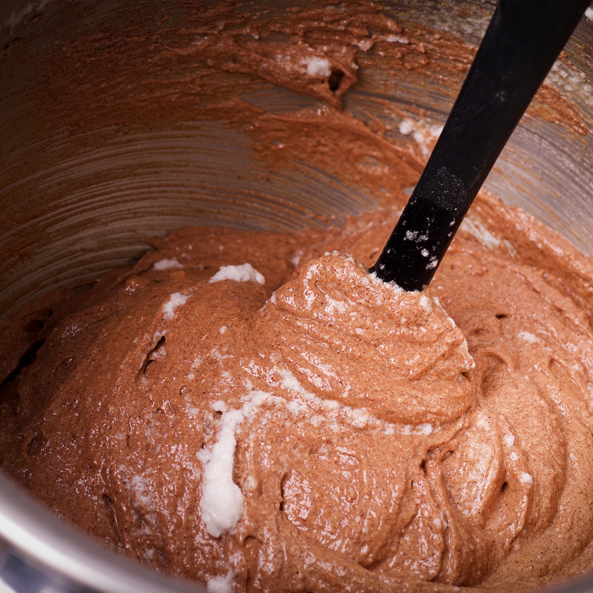 Someone using a rubber spatula to gently stir beaten egg whites into chocolate almond cake batter.