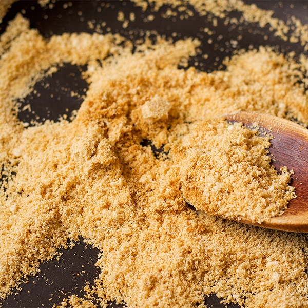 Someone using a wood spoon to stir a skillet filled with toasted almond flour.