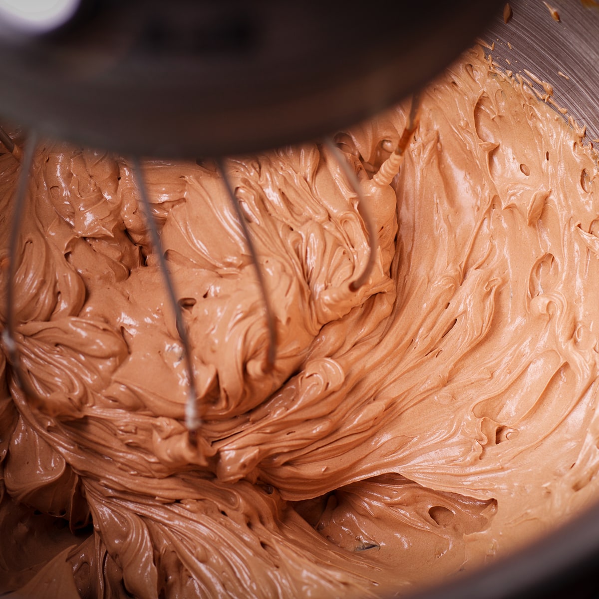 Looking down into the bowl of an electric mixer while it beats chocolate orange buttercream.