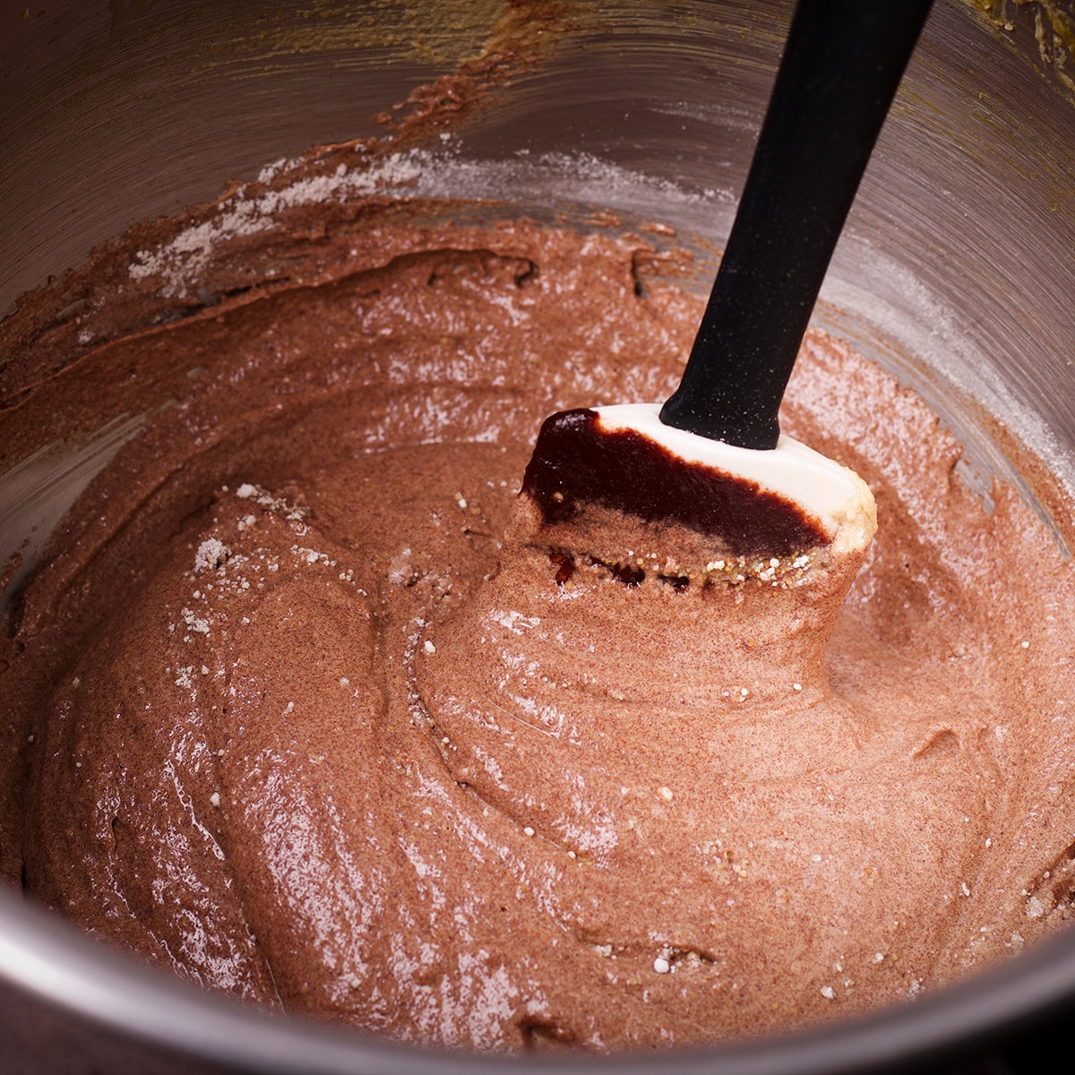Someone using a spatula to stir melted chocolate into chocolate almond cake batter.