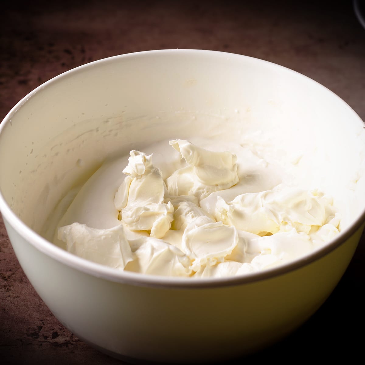 A white bowl filled with whipped cream and pieces of cream cheese.