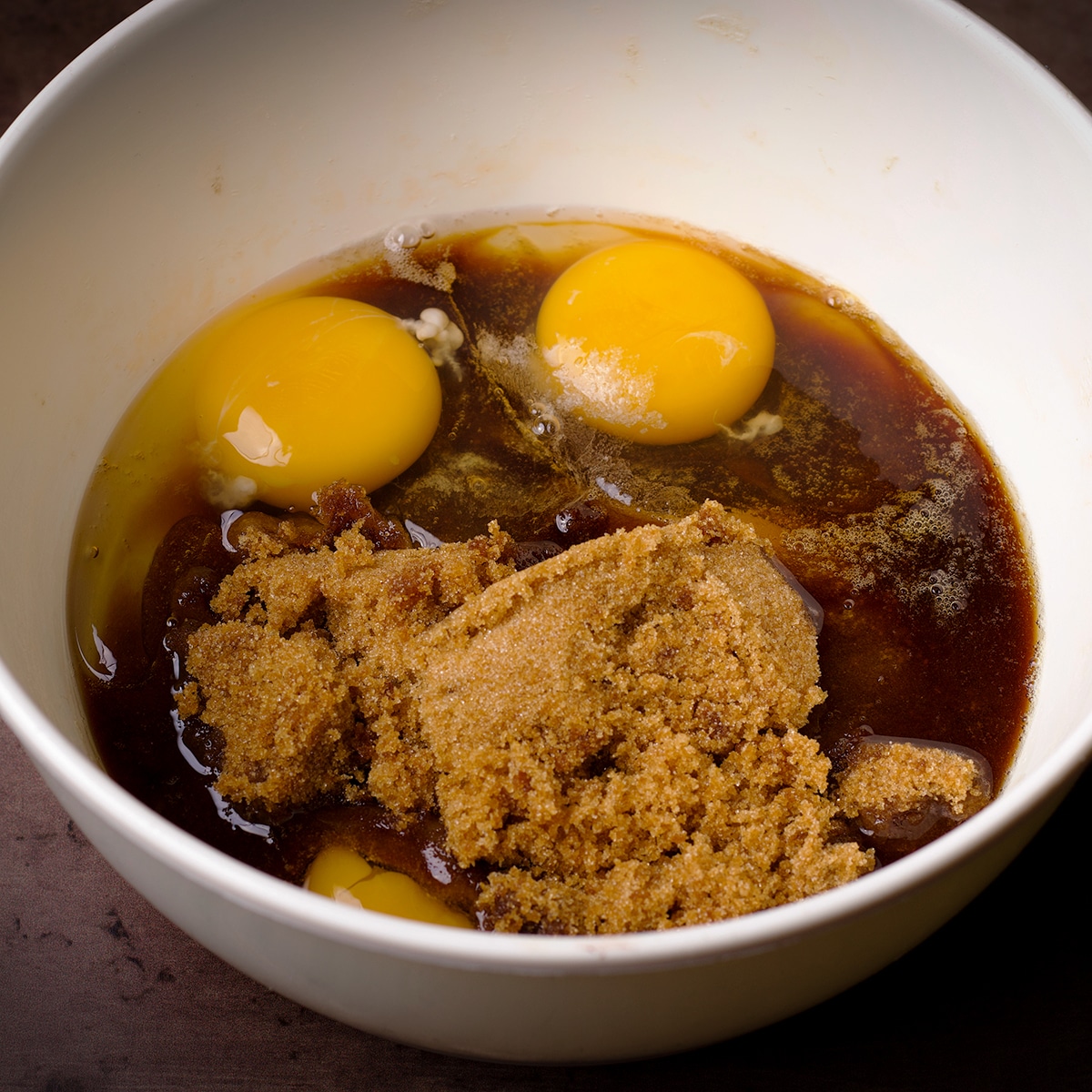 A bowl containing brown sugar, eggs and vanilla.