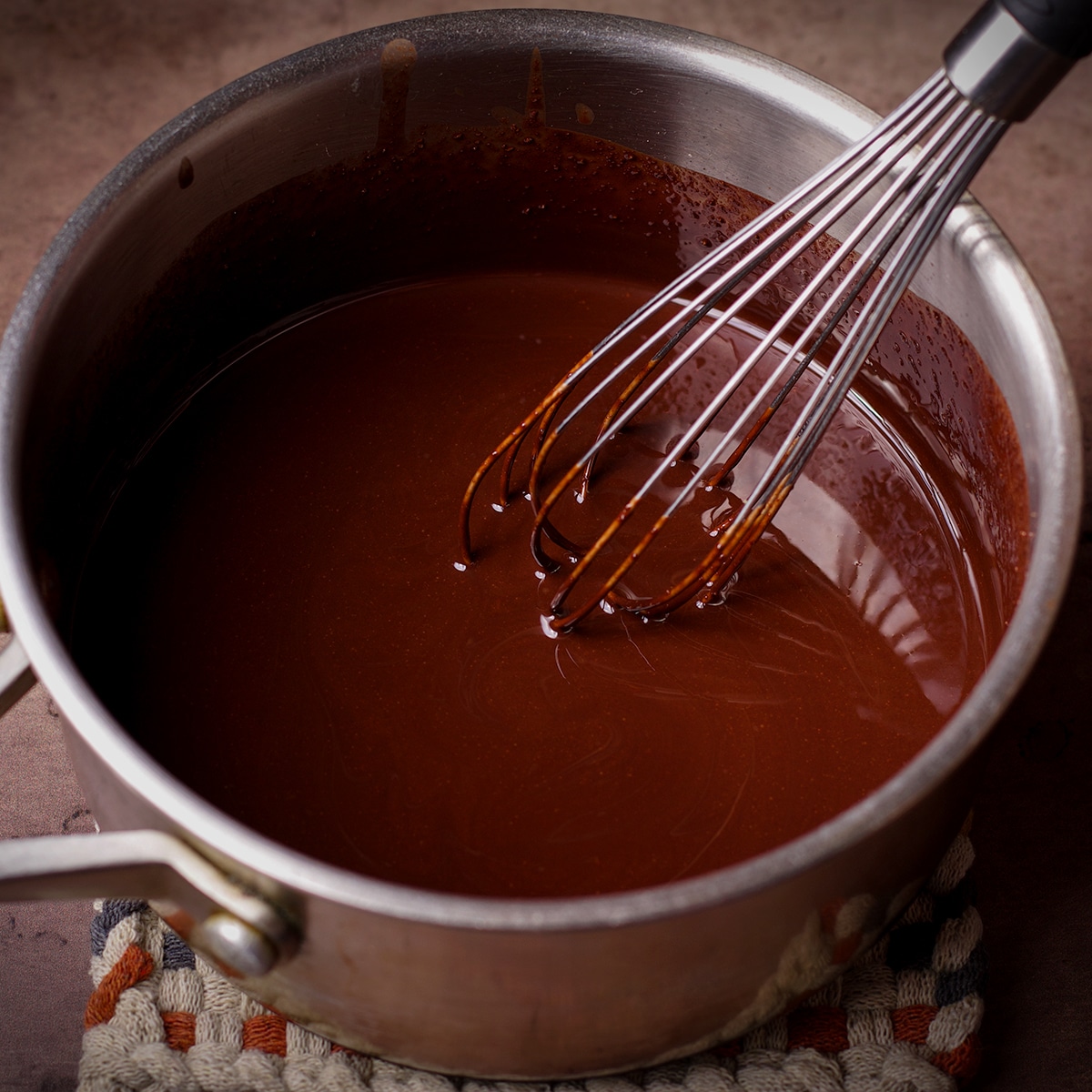 Someone using a wire whisk to stir a pan of melted chocolate.