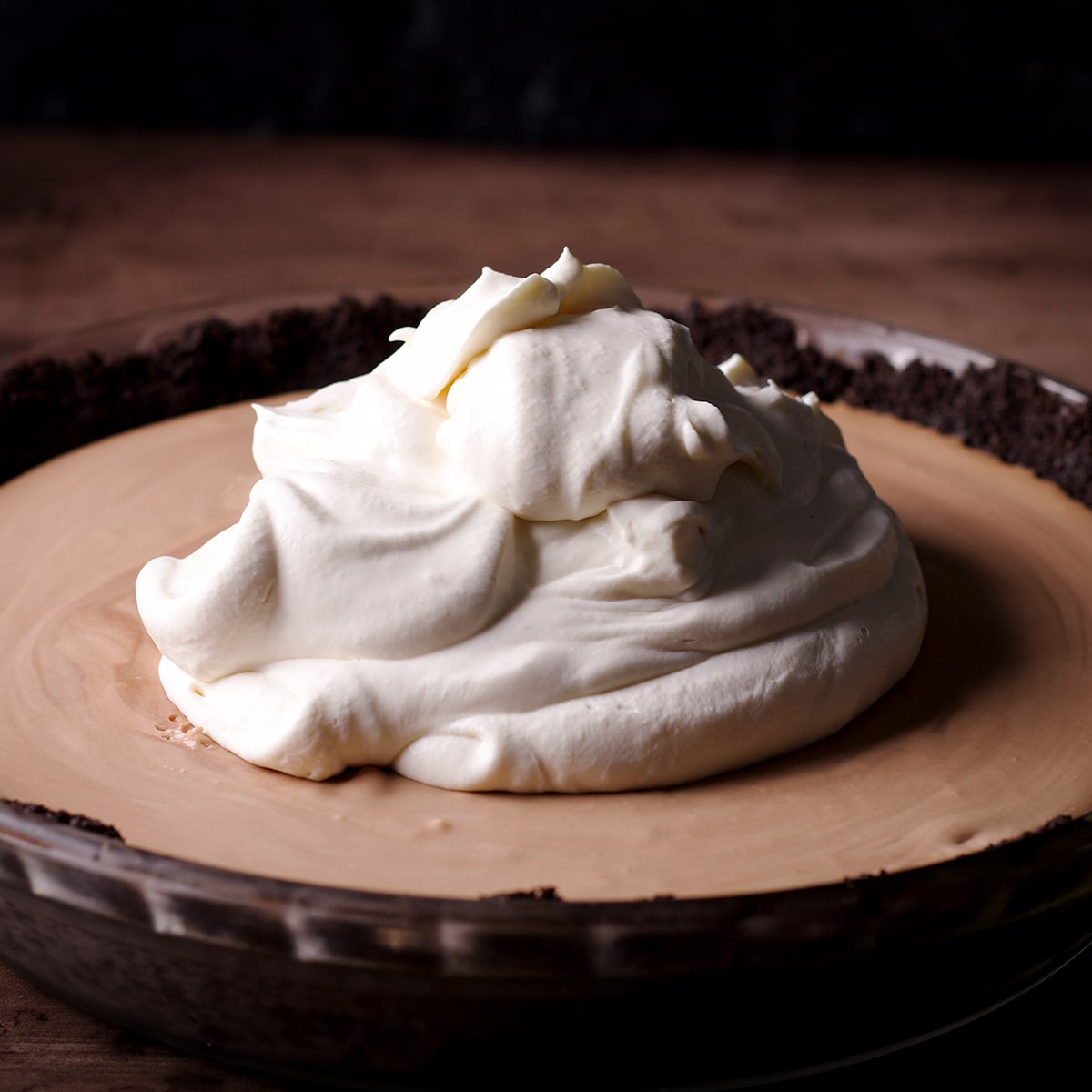 A large dollop of whipped cream onto of a chocolate mousse pie with an Oreo cookie crust.