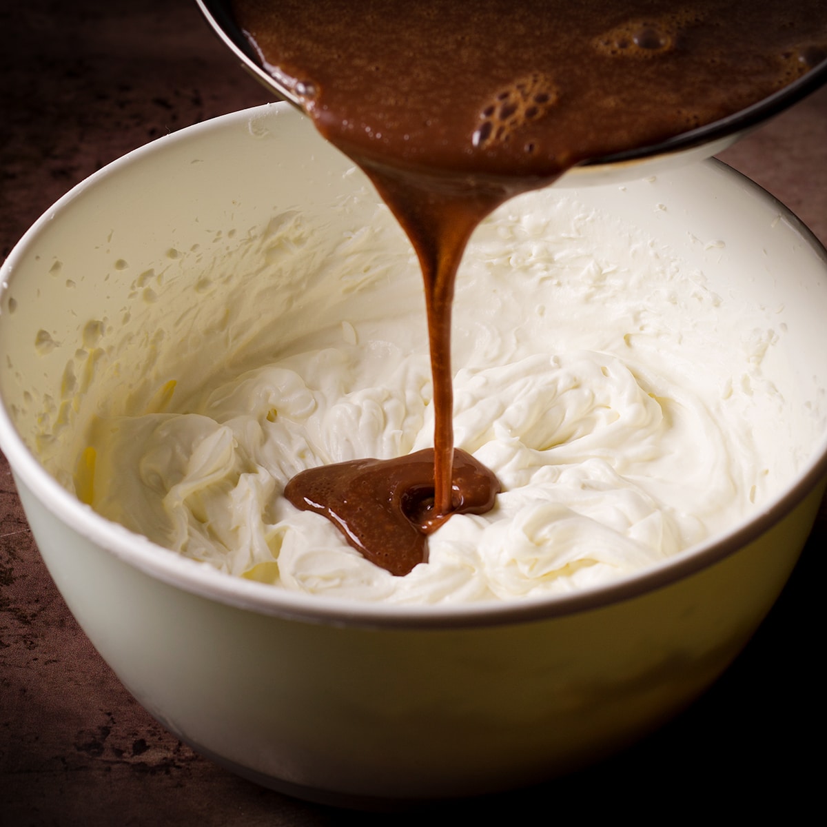 Pouring hot milk chocolate ganache into whipped cream.